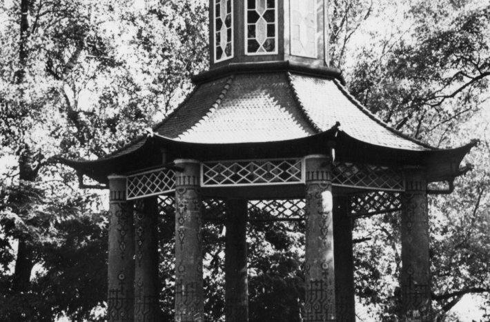 Altana chińska. Do dokoła niej drzewa. W lewym dolnym rogu kobieta idzie ścieżka. Perspektywa sprawia, że kobieta wydaje się mikroskopijna.