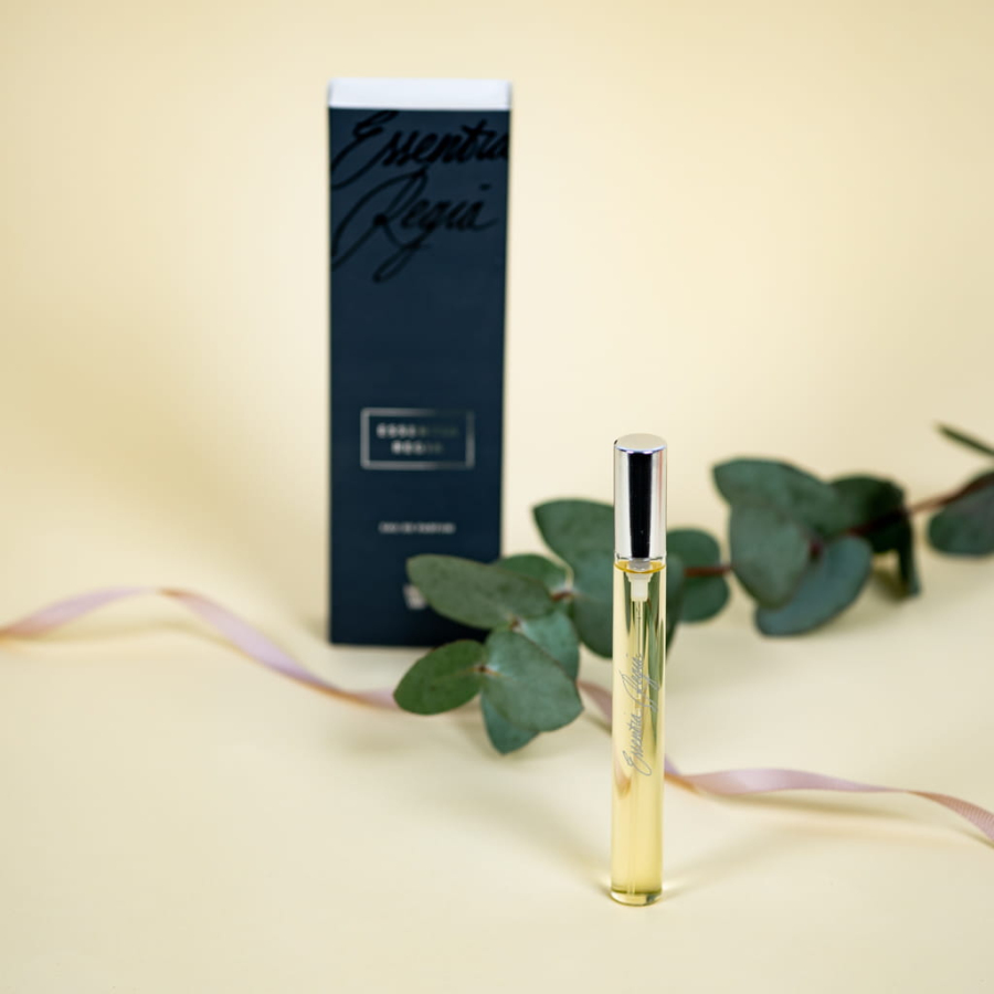 Zdjęcie przedstawia perfumy w wąskiej butelce i pudełko  w kolrze granataowym. Na jasno żółtym tle leży różowa wstążka i sucha gałązka z kwiatami.