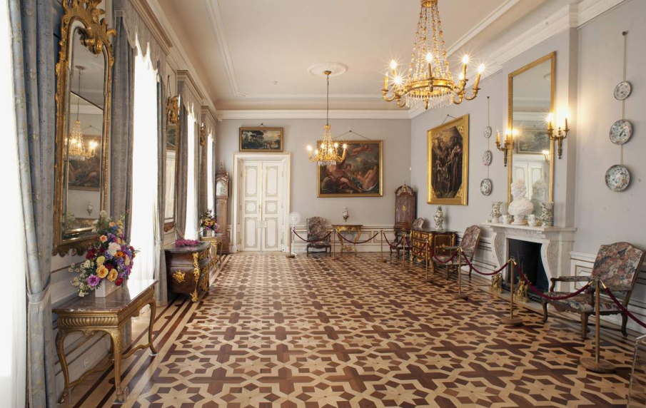 Duże wnętrze pałacowe w Wilanowie, z kolorową posadzką, meblami antycznymi i dziełami sztuki na ścianach.